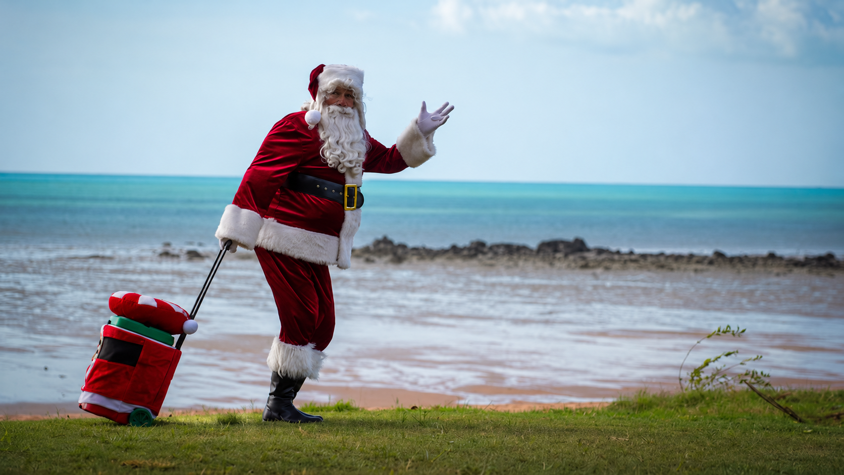 Santa walking beside the turquoise water at Broome Town Beach with his festive trolley.